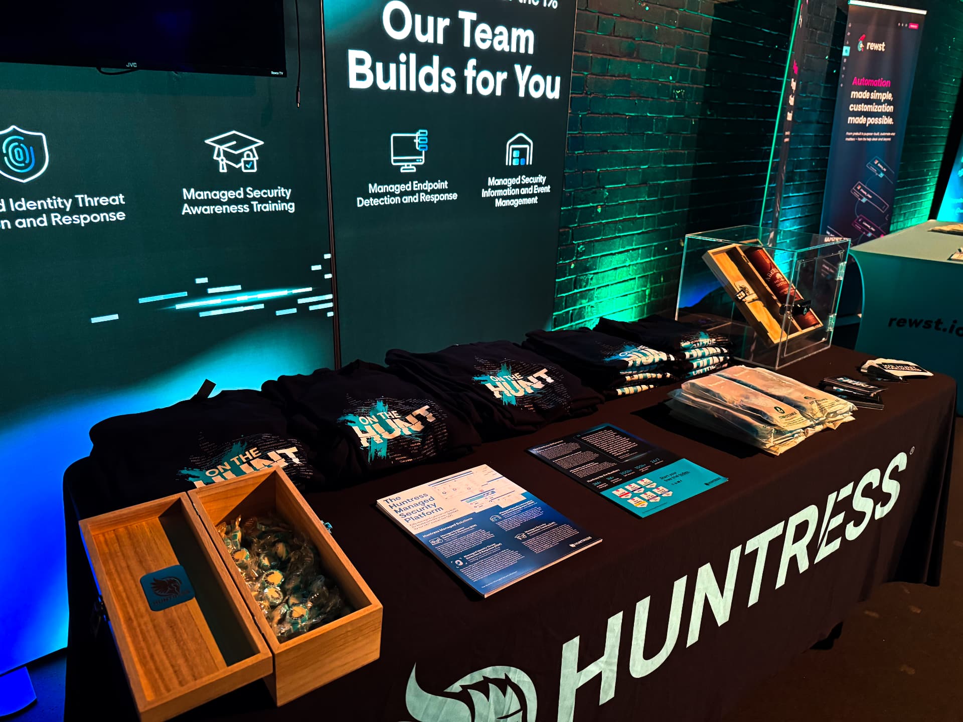 Huntress event table with branded merchandise: black t-shirts, wooden presentation boxes and printed collateral